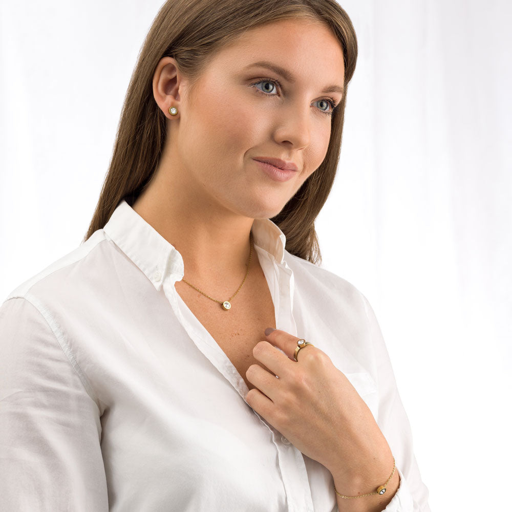 Lady wearing a collection of Blomdahl Gold Grand Bezel jewellery set consisting of earrings, necklace, bracelet and ring medical sensitive skin friendly nickel free