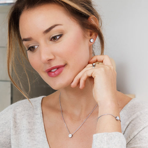 A collection of Silver Grand Bezel jewellery, consisting of a pair of earrings, necklace and ring. Bracelet is on her right hand.Grand Bezel is a an elegant jewellery design from Blomdahl that comes with a 8mm Swarvoski crystal in the middle medical sensitive skin friendly nickel free